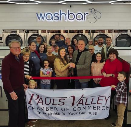 Josh and Hannah Chapman (front row, center), owners of the Washbar, were welcomed as new Pauls Valley Chamber of Commerce members with a ribbon cutting celebration Tuesday. The laundromat offers coin/card self serve, as well as full-service wash and fold laundry drop-off and press and starch service for both commercial and residential customers. The Washbar, at 500 S. Chickasaw St., is open from 8 a.m. to 9 p.m. seven days a week. Courtesy photo