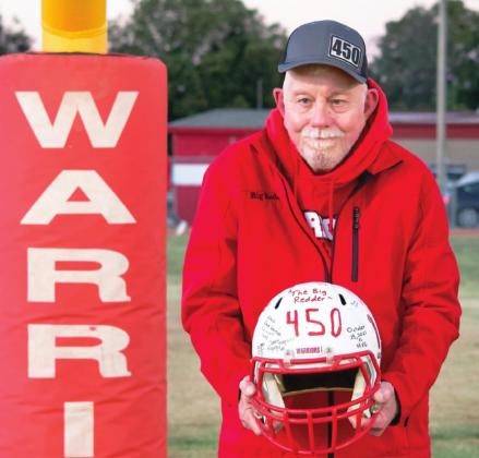 Maysville's Roger Perrin poses with a signed helmet the Maysville Warrior football team presented him to mark his 450th consecutive Maysville game earlier this season. His hat, emblazoned with 450 to commemorate the accomplishment, was custom-made for him by Tamara Tadlock of Elmore City.