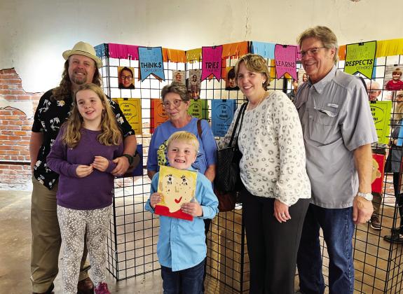 Owen Luker (center) poses with his self-portrait and his family during the “Characteristics on Canvas” art show at The Vault in downtown Pauls Valley Tuesday evening. The show featured self-portraits by students in Erica Shippey’s first grade class at Whitebead School. Each piece included a statement from the artist describing a skill, ability or personality trait that makes them uniquely them. The project was made possible by a grant from the Pauls Valley Foundation for Academic Excellence.